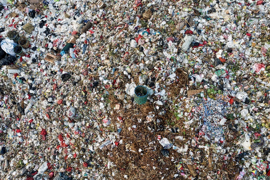 A large, uncontained heap of mixed household and commercial rubbish spread across an outdoor area, consisting primarily of crumpled paper, plastic wrappers, cardboard pieces, and scattered food packag