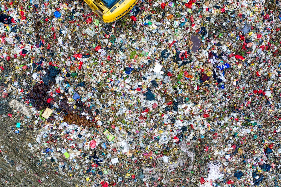 A large, uncontained heap of mixed household and commercial rubbish spread across an outdoor area, consisting primarily of crumpled paper, plastic wrappers, cardboard pieces, and scattered food packag
